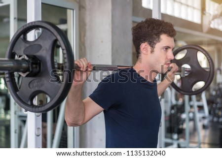 Handsome weightlifter lifting barbells with Squats smith machine working out in the fitness gym.