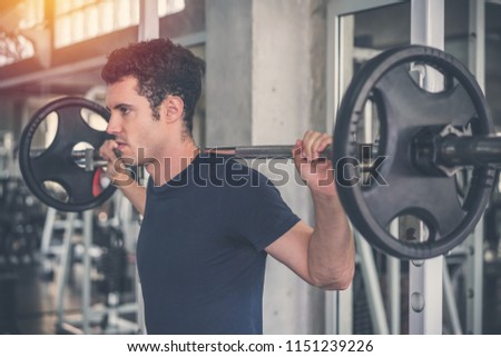 Handsome weightlifter lifting barbells with Squats smith machine working out in the fitness gym.