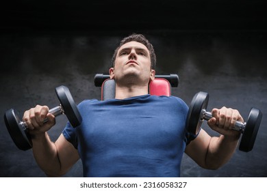 Handsome weightlifter lifting bench press working out with dumbbell in the gym