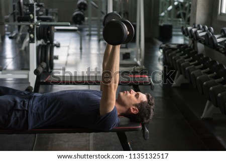 Handsome weightlifter lifting bench press working out with dumbbell in the gym.