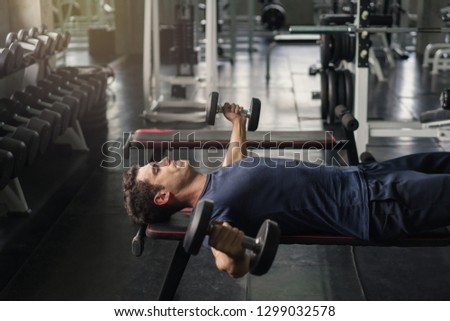 Handsome weightlifter lifting bench press working out with dumbbell in the gym.