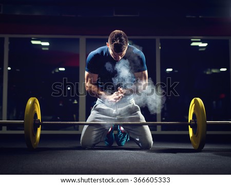 Handsome weightlifter preparing for training. Shallow depth of field, selective focus on hands and dust.