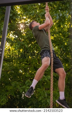 Handsome and well b uild guy is doing climbing the rope exercise