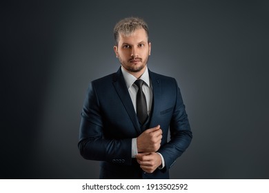 A handsome well-groomed man in a business suit stands on a gray background. Concept businessman, business communication