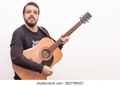 Handsome White Hispanic Latin Adult Male With Short Beard, Short Hair, Black Dress And Glasses Posing Holding His Acoustic Guitar On White Background