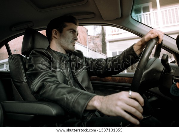 handsome white man driving luxury car wearing\
leather jacket. A stylish male model with status and elegance\
shifts gears, and drives through the city.\
