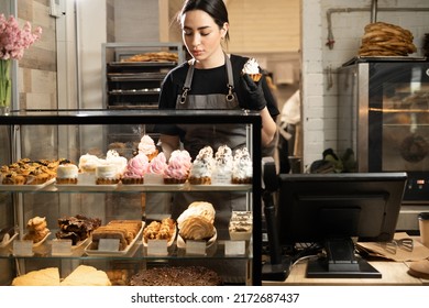 Handsome woman coffee shop employee placing pastry and cake in bakery refrigerator showcase at cafe. Small business, part time job concept