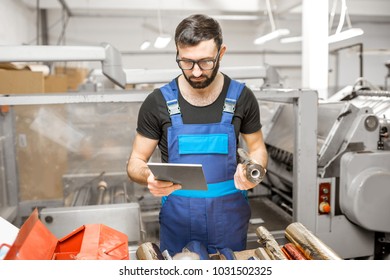 Handsome worker holding cliche and foil roll for stamping standing at the vintage printing manufacturing - Shutterstock ID 1031502325