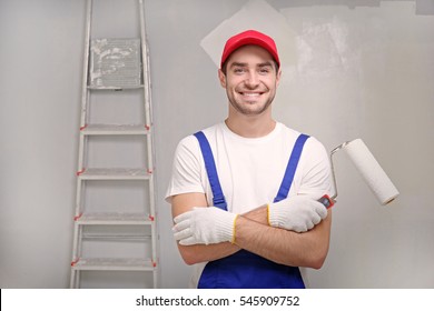 Handsome worker with paint roller in empty room