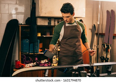 Handsome Worker Waxing Ski With Wax Iron In Repair Shop