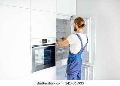 Handsome Workman Installing New Refrigerator In The Modern Kitchen At Home