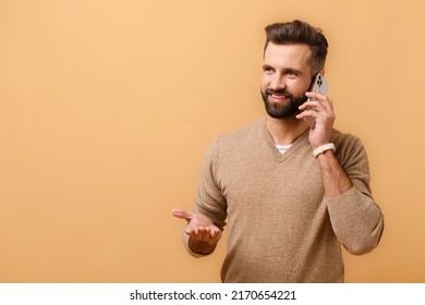 Handsome young 30s man talking phone, calling to discuss plans, looking away with dreamy facial expression. Indoor studio shot isolated on beige background