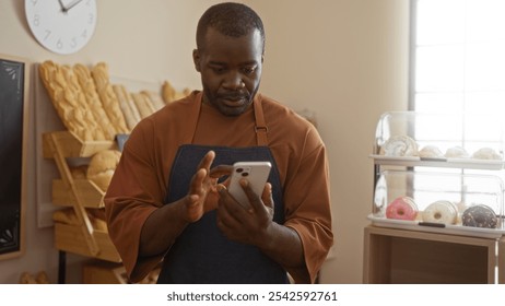 Handsome, young, african, american, black, man using a smartphone in a bakery, surrounded by indoor shelves of fresh bread and pastries in a cozy shop interior - Powered by Shutterstock