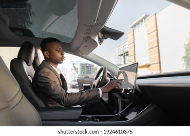 Handsome Young African American Businessman Touches The Touchscreen In His New High-tech Electric Vehicle While Drinking Take Away Coffee Near City Trade Mall. Self Driving Vehicle Concept