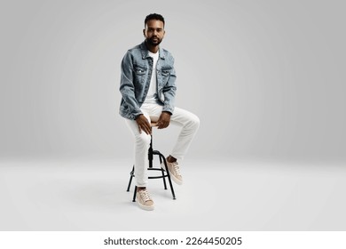 Handsome young african american guy sitting on stool, posing in studio - isolated. - Shutterstock ID 2264450205