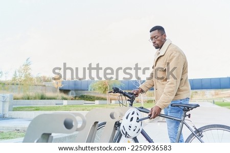 Handsome young African college student parking his bicycle. He is wearing blue jeans and a jacket. Bike as conveyance at the university campus.