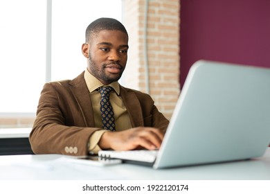 Handsome Young African Man In Suit At Table In Office With Laptop 