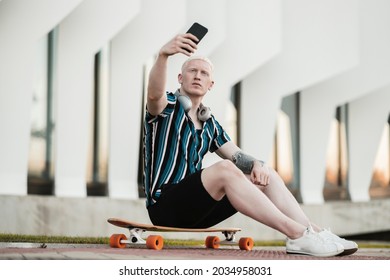 handsome young albino boy, in the city with skateboard using smartphone - Powered by Shutterstock