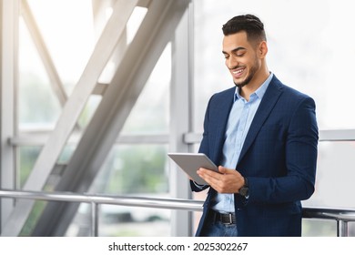 Handsome Young Arab Businessman Using Digital Tablet While Waiting At Airport Terminal, Smiling Middle Eastern Man Working Online Or Browsing Internet On Tab Computer, Enjoying Modern Technologies