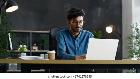 Handsome Young Arab Busy Male Office Worker Sitting At Table And Working On Laptop Computer.