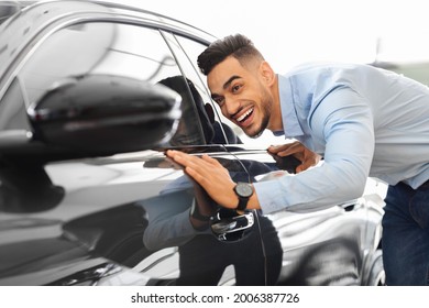 Handsome Young Arab Man Buying New Car, Standing At Car Salon And Checking Automobile Surface, Closeup. Smiling Middle-eastern Guy Looking At Beautiful Black Auto In Showroom