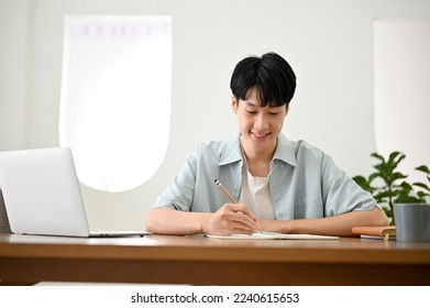 Handsome young Asian male college student focusing on his homework, taking notes or making lists on a paper. - Powered by Shutterstock