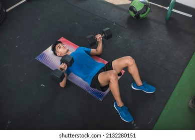 A Handsome Young Asian Man Does Dumbbell Floor Presses At An Old Gym. Chest And Upper Body Workout. Active Fitness Lifestyle For Youth.