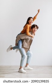 Handsome young Asian man giving piggyback ride to his girlfriend against white studio wall, full length portrait. Millennial couple having fun, spending romantic times together - Shutterstock ID 2090139835