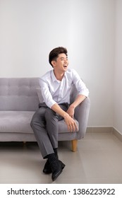 Handsome Young Asian Man Sitting At Home On Sofa, Smiling Happy, Looking At Camera.