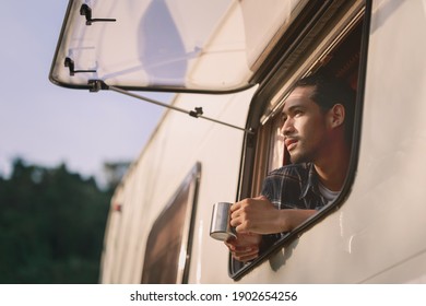Handsome young Asian man, traveler on road trip, sit inside camping van in the morning. Cosy comfortable setup in camper trailer or van. Millennial travel trend, adventure on the road.