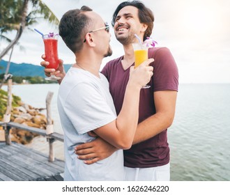 Handsome Young Attractive Male Couple, Gay Couple And Family, Valentine's Day At A Tropical Resort With Cocktails In Their Hands