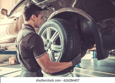 Handsome young auto mechanic in uniform is changing a tire while working in auto service - Powered by Shutterstock