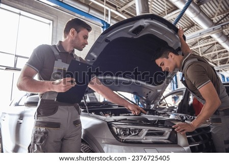 Handsome young auto mechanics in uniform are examining car while working in auto service