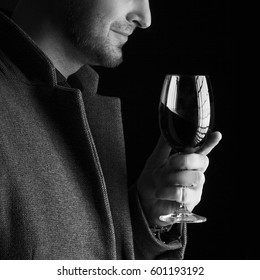 Handsome young bald man smelling red wine before tasting and drinking it. Man wearing spring coat and holding a glass of red wine in his hand. Low key portrait. Black and white