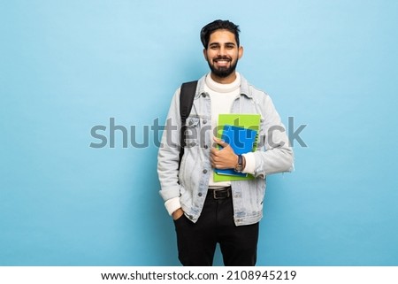handsome young bearbed indian man with backpack hold books in studio background