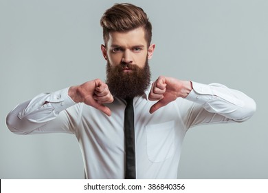 Handsome Young Bearded Businessman In Classic White Shirt Is Showing Not Ok Sign, On A Gray Background