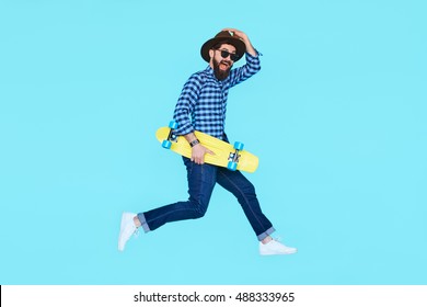 Handsome young bearded man jumping with yellow skateboard against the colorful wall. Hipster with beard in motion on blue background - Powered by Shutterstock