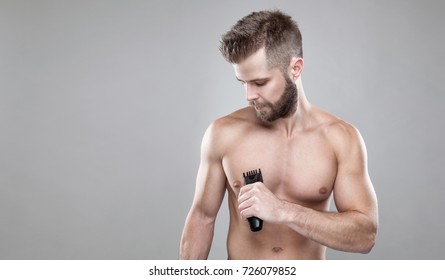 Handsome Young Bearded Man With A Trimmer Shaving Off Body Hair