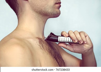 Handsome Young Bearded Man With A Trimmer Shaving Off Body Hair