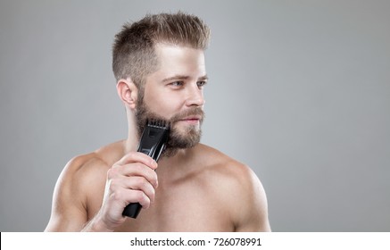 Handsome young bearded man trimming his beard with a trimmer