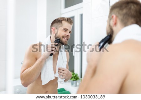 Handsome young bearded man trimming his beard with a trimmer