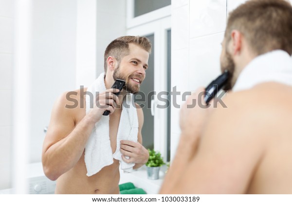 Handsome young bearded man trimming his beard\
with a trimmer