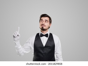 Handsome Young Bearded Restaurant Host In Elegant Outfit With Bow Tie Pointing Up Against Gray Background