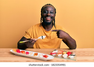 Handsome Young Black Man Eating Sushi Sitting On The Table Smiling Happy Pointing With Hand And Finger 