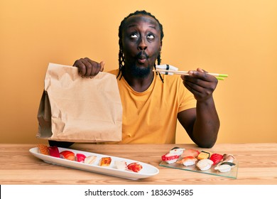 Handsome Young Black Man Eating Take Away Sushi Sitting On The Table Making Fish Face With Mouth And Squinting Eyes, Crazy And Comical. 