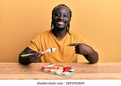 Handsome Young Black Man Eating Sushi Sitting On The Table Smiling Happy Pointing With Hand And Finger 