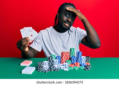 Handsome Young Black Man Playing Poker Holding Cards Stressed And Frustrated With Hand On Head, Surprised And Angry Face 