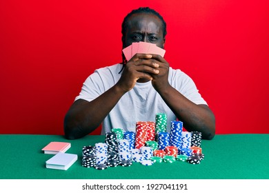 Handsome young black man playing gambling poker covering face with cards skeptic and nervous, frowning upset because of problem. negative person. 