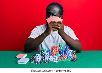 Handsome Young Black Man Playing Gambling Poker Covering Face With Cards Skeptic And Nervous, Frowning Upset Because Of Problem. Negative Person. 