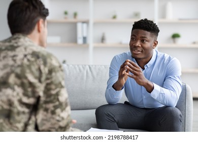 Handsome Young Black Man Professional Psychotherapist Meeting With Veteran Unrecognizable Guy Wearing Camouflage Uniform, Helping Soldier With Reintegration After Coming Back Home, Clinic Interior